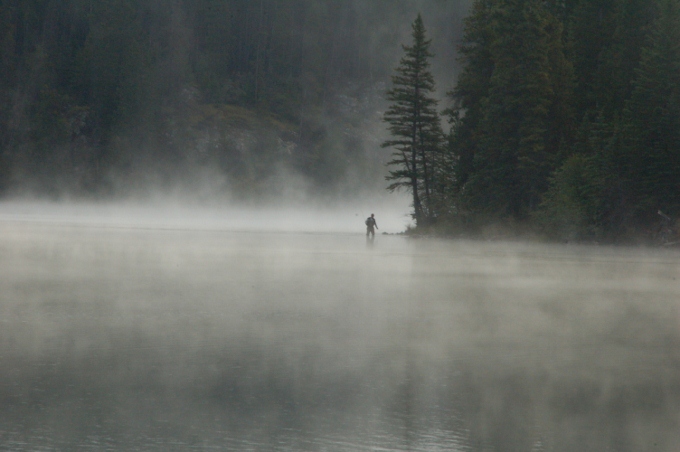 a lone fisherman is seen through the mist as it rises from the lake in Jasper NP, Canada